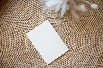Summer stationery still life. Closeup of blank card mock-up with dry leaf in boho interior. Grunge beige concrete background. Flat lay. Moody boho design