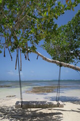 Paradise at the beach with a hammock in the caribbean blue ocean and a wooden swing in the sand tightened on a palm tree, perfect place for the holiday to relax and chill in mahahual mexico