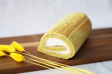 Close-Up Of Matcha (green tea flavor) Cake Roll (Swiss Roll) on Wooden board with yellow flowers decoration.