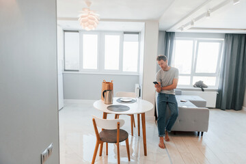 Young man in casual clothes is indoors controlling smart home technology