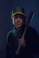 Shaded dark portrait of a blond man with stubble beard and baseball cap in a dark green wool...