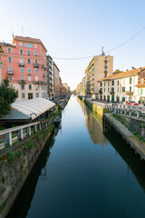 Fototapeta na wymiar Perspective of the famous old Navigli neighborhood, Milan, Italy. Water canal in the foreground, looking like a river. Buildings and blue sky in the background.