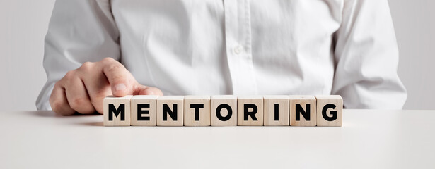 Man pressing his finger on the wooden cubes with the word mentoring.