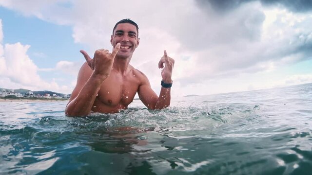 Brazilian surfer. Surfer sits on surf board in the water and shows the Shaka sign with splash at Campeche surf spot on Santa Catarina island in Brazil