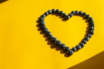 Obraz premium Healthy food, raw food diet. Blueberries in the shape of a heart on a yellow background. Hard shadows. Love symbol.
