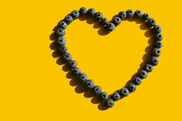 Obraz premium Healthy eating. In the sunshine. Blueberries in the shape of a heart on a yellow background. Hard shadows. Love of raw food.