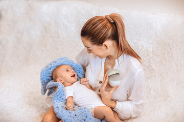 Mother smiling to her newborn baby and holding the bottle of milk. Copy space.