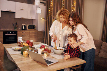 Cheerful people having happy weekend. Family of mother, daughter and son is on the kitchen at evening time