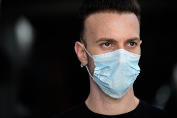 Close-up portrait of young handsome man wearing face mask to protect from corona virus outdoors while thinking