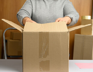 woman in a gray sweater is packing brown cardboard boxes on a white table