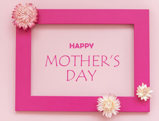 Creative arrangement of flowers on pink background with happy Mothers day text. Flat lay.