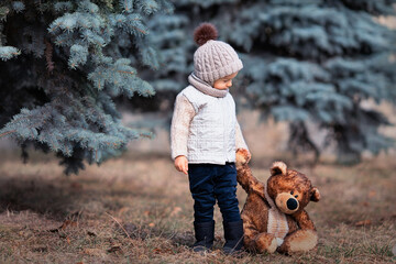 Baby and his friend bear in the park. Winnie the Pooh. Spring walk of a child with a toy. Based on a fairy tale. Brown teddy bear and a boy in a knitted hat and jacket