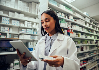 Woman in chemist wearing labcoat checking medicine details in digital tablet
