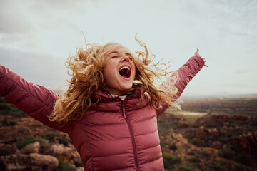 Close-up of a beautiful woman on mountain trail with her hair flying and hands outstretched with...