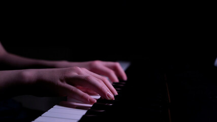 Piano in the dark. A ray of light falls on the keys. Pianist's hands. Image with selective focus