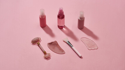 Rose quartz facial massage tools gua sha stone scrapers, face roller and beauty products in plastic bottles isolated on pink surface