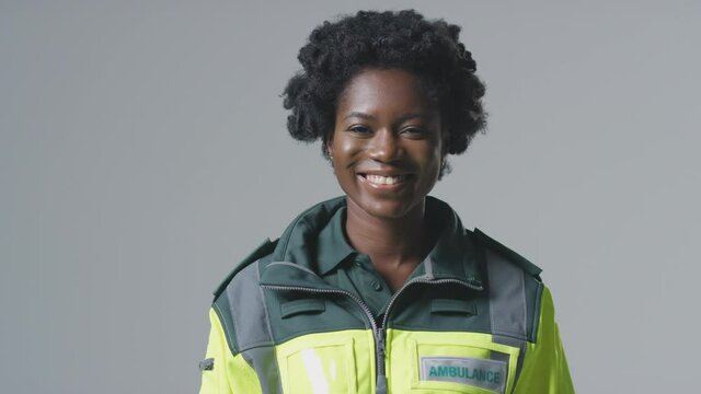 Smiling young female paramedic wearing uniform in front of plain studio background - shot in slow motion