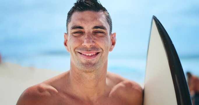 Brazilian surfer stands with surf board on the beach looks into the camera and smiles