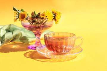 A cup of tea with a bouquet of dandelions on a yellow background, a place for text