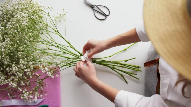 people, gardening and floral design concept - close up of woman arranging flowers and tying bow at home