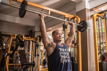 A buff and rugged asian man does Seated Military Presses. Shoulder workout at the gym.