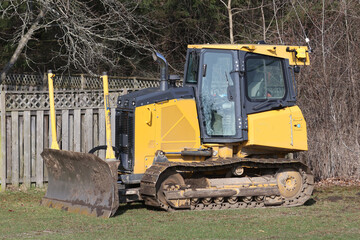 Fototapeta na wymiar Small Junior sized bulldozer parked in back yard about to help clear land for builidng houses 