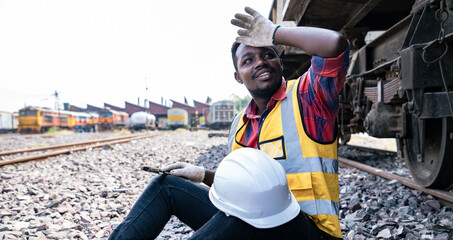 Portrait of Africa American engineering man wear hardhat and relax near steel container before hard work in front of train garage. Technician and Railway Engine and Parts Repair