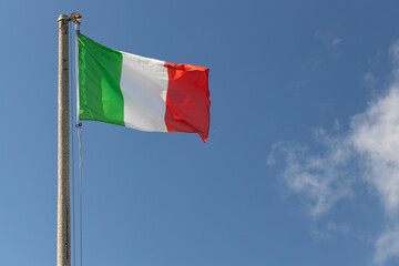 Fototapeta na wymiar Italian flag blowing in the wind in the blue sky