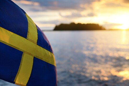 Flag of Sweden on a private vessel (yacht). Golden sunset clouds blurred in bokeh. Sailing in Mälaren lake. Patriotism, national identity, symbol, independence, politics