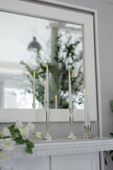 white candles with fire in silver candlesticks on a white fireplace