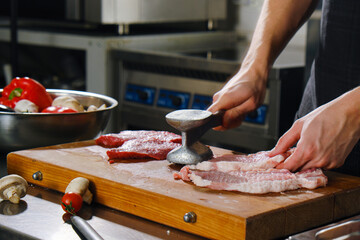 The chef beats a piece of meat with a metal hammer. Cooking entrecote or steak. The cook in the kitchen in the restaurant.