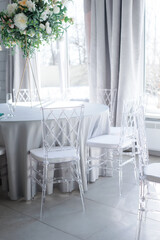 transparent plastic chairs at a round table with a blue tablecloth indoors