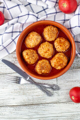 Meatballs in tomato sauce in a bowl on wooden table.