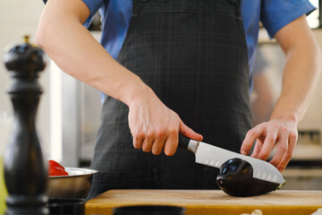 The male Caucasian chef cuts vegetables, peppers, tomatoes and eggplants on a wooden cutting board.