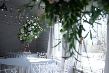 A large, tall arrangement of artificial flowers in white and peach on an empty table with a blue tablecloth. White room, sunny day.