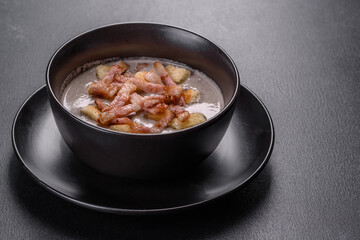 Fresh delicious hot puree soup with mushrooms and bacon in a black plate