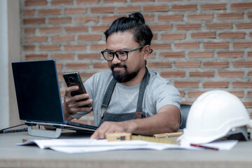 Male architect or engineer working at home drawing the construction project, An architect working on a laptop using a mobile phone on the working desk. Business and Technology concept