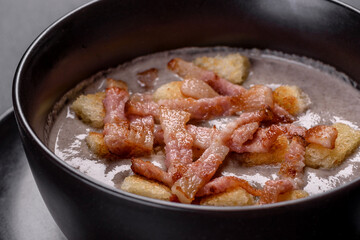 Fresh delicious hot puree soup with mushrooms and bacon in a black plate