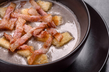 Fresh delicious hot puree soup with mushrooms and bacon in a black plate
