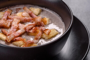 Fresh delicious hot puree soup with mushrooms and bacon in a black plate