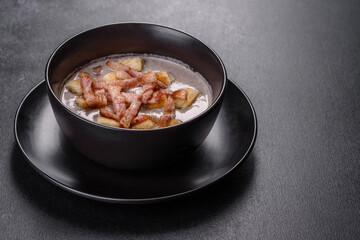 Fresh delicious hot puree soup with mushrooms and bacon in a black plate