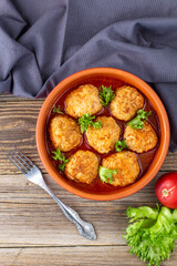 Meatballs in tomato sauce in a bowl on wooden table.