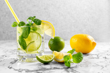 Citrus lemonade with ice in a glass decorated with lemon, lime and mint slices and on a on a marble table. Fresh summer drink. Detox. Healthy food rich in vitamins and antioxidants. Copy space