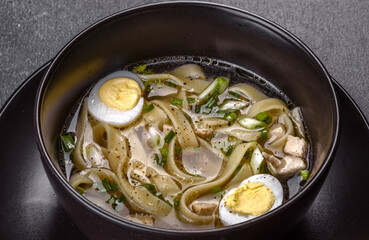Fresh delicious hot soup with noodles and quail egg in a black plate