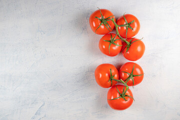 seven red fresh and tasty tomatoes on a green twig on a white stone background. Top view.