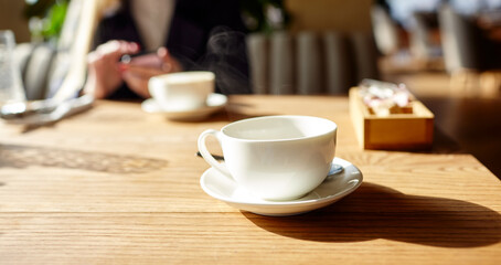 Cup of coffee on the table. Woman typing text message on smart phone in a cafe. Young woman sitting at a table with a coffee using mobile phone. Coffee break.  Blurred image, ..selective focus