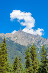 Scenery of high mountain peak over blue sky with white clouds and green foreground.