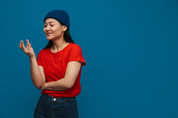 Asian teen girl in hat smiling and rubbing her fingers