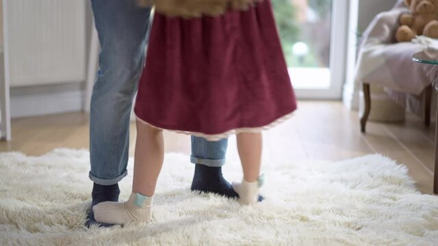 Legs of little girl stepping on man's feet and dancing. Unrecognizable Caucasian daughter dance with father indoors at home. Family relationship and leisure concept
