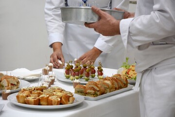 The chef and the waiter are setting the table with appetizers for the event.